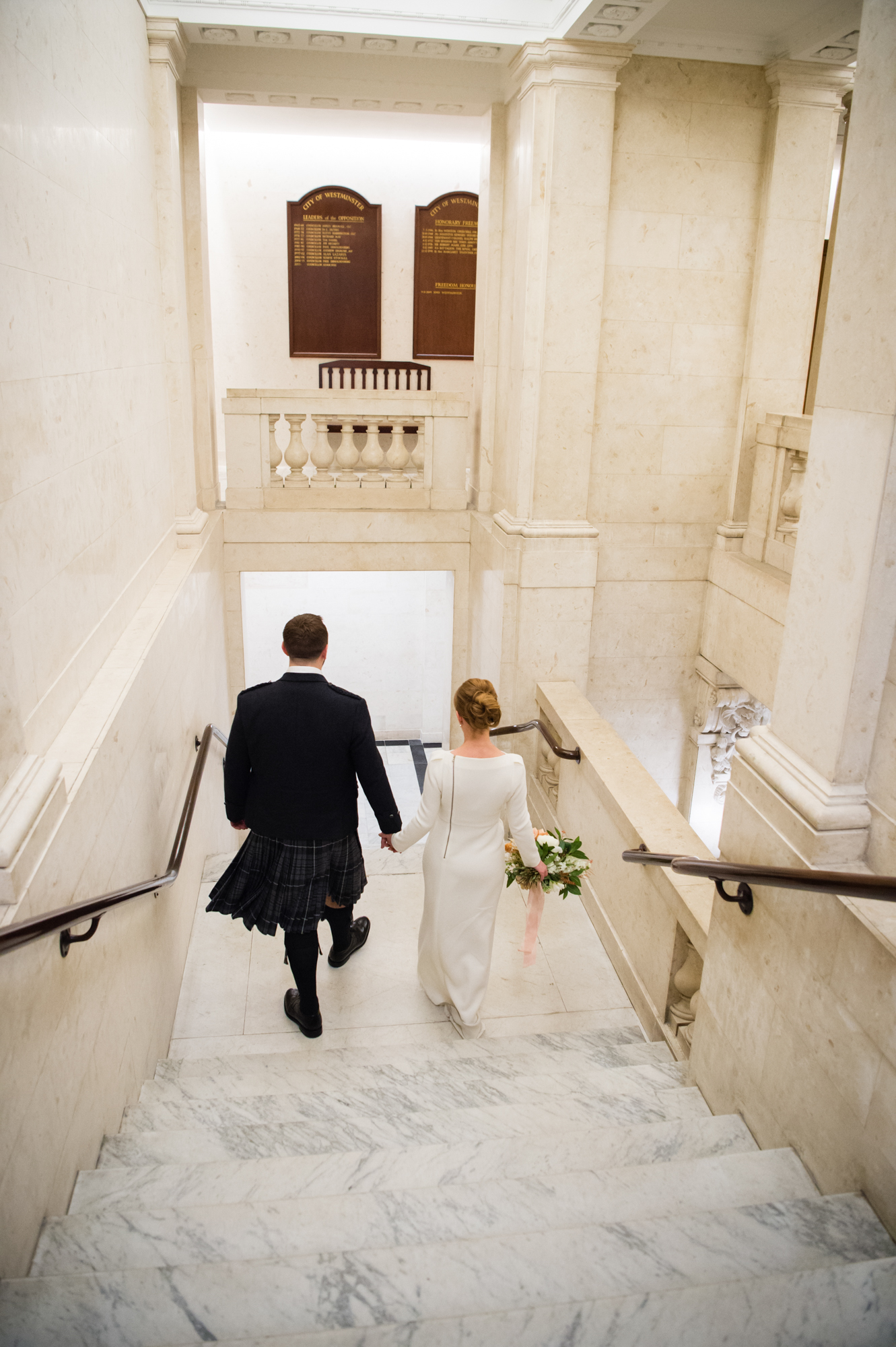 A newly married couple walking down the marble steps inside Marylebone Town Hall